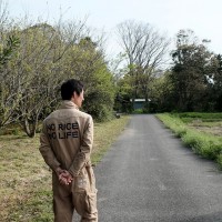 農園の周囲を案内してくれた「つるかめ農園」オーナーの鶴渕真一さん。「NO RICE NO LIFE」とプリントされたつなぎは、友人のTシャツブランド「米T」のもの